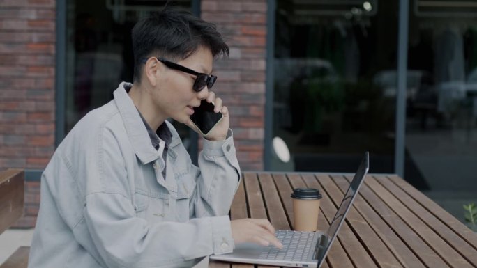 亚洲商人在城市的露天咖啡馆里用手提电脑打电话讨论项目
