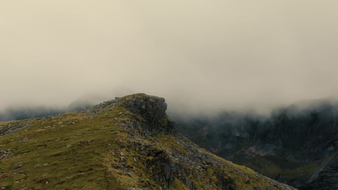 无人机在史诗般的岩石峡湾峰周围飞行，背景是浓密的云层