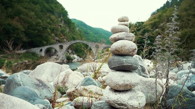 平衡与和谐。禅宗石和鹅卵石相互平衡地堆叠在一起，形成了一座塔，背景是一座石桥的拱门