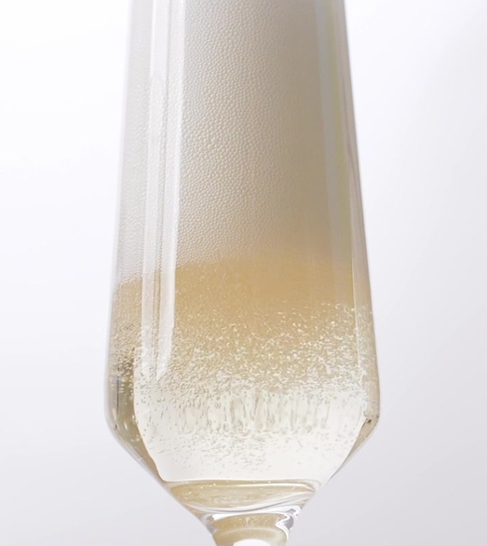 将香槟酒倒入一个透明的玻璃杯中，让许多气泡漂浮起来，奢华地散发着金色的光芒。