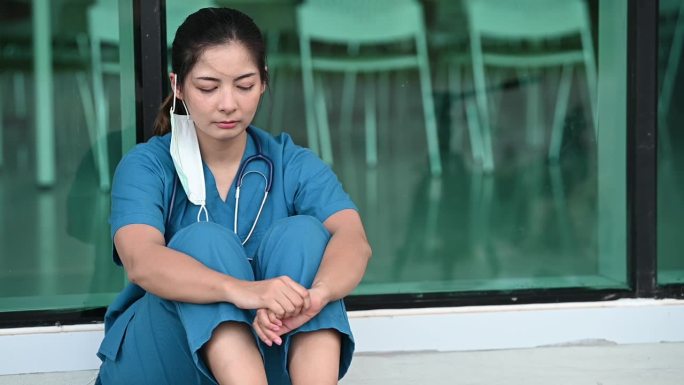 疲惫沮丧的亚洲女磨砂护士戴着口罩蓝色制服坐在医院地板上