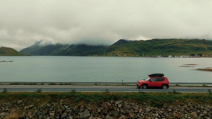 无人机跟随一辆红色SUV沿着海岸公路行驶，背景是风景如画的斯堪的纳维亚风景