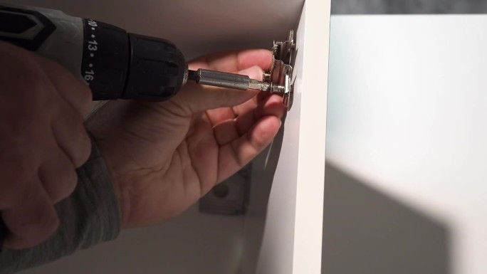 使用电动螺丝刀安装家具门铰链。