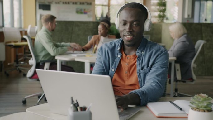 英俊的非裔美国企业家在现代办公室里用笔记本电脑和耳机听音乐