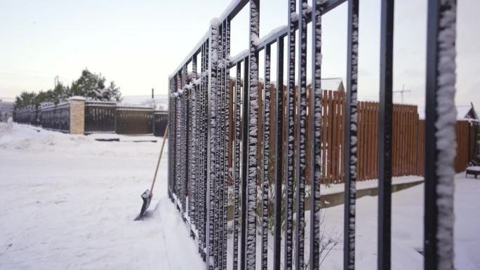 街上的第一场雪，雪地里的乡间小屋和篱笆。白雪覆盖的黑色金属栅栏。清除街道积雪的概念，用铲子。