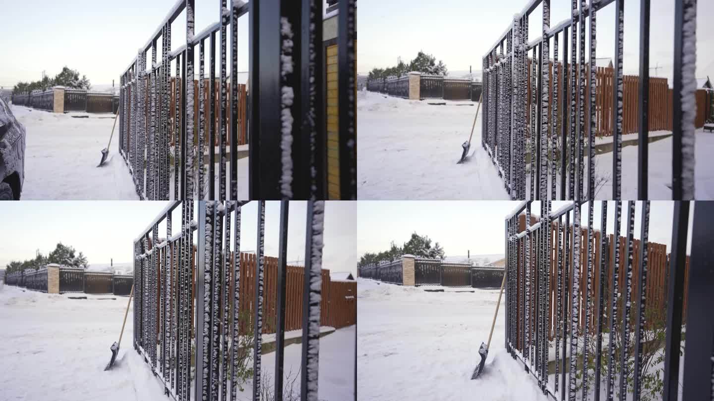 街上的第一场雪，雪地里的乡间小屋和篱笆。白雪覆盖的黑色金属栅栏。清除街道积雪的概念，用铲子。