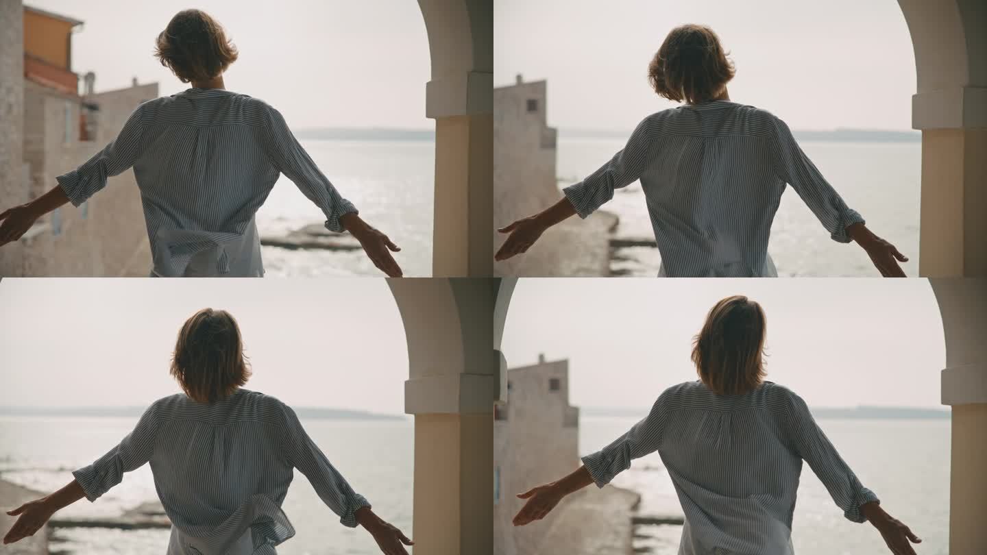 在克罗地亚，女游客站在海边的建筑里，在晴朗的天空下，伸开双臂享受着风