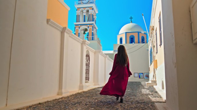 在圣托里尼，一个穿着红裙子的漂亮女孩正走向有大钟的大教堂。