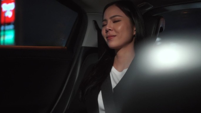 商务女性坐在汽车后座系上安全带，晚上看着窗外的放松感觉。开车的女人在去目的地的路上坐出租车。