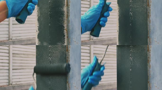 用灰色防腐漆对锈柱进行喷涂。戴着手套拿着油漆滚筒的手。外部维修。