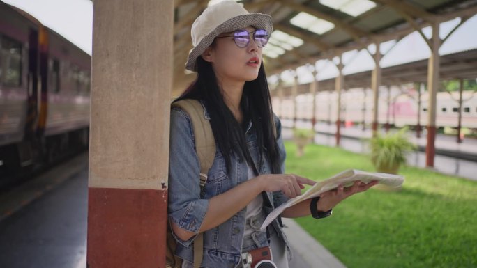 快乐的年轻亚洲女性独自站在火车站，查看纸质地图，找出自己的目的地