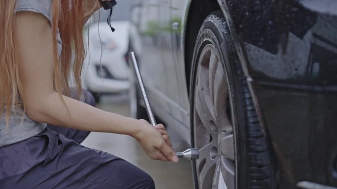 一个女人的汽车轮胎有问题，所以她试着在雨中修理它