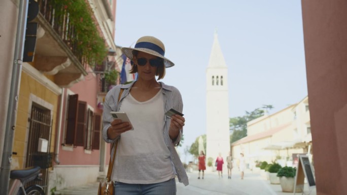 克罗地亚，女游客用信用卡和智能手机散步，背景是罗维尼教堂