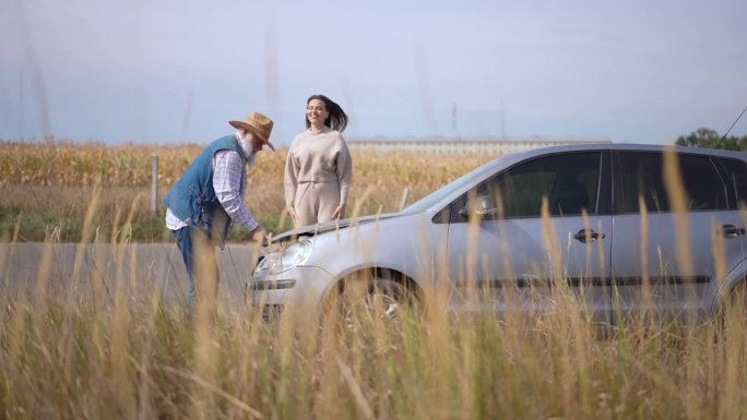 广角镜头，高兴的妇女感谢老人帮忙修理坏了的汽车。开心兴奋的白人女士跳起来拥抱农民，在户外盖上兜帽。