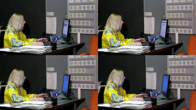 电器工厂的插座打开了背景，一位白人女士坐在办公桌前用笔记本电脑工作。女商人在电脑上打字。