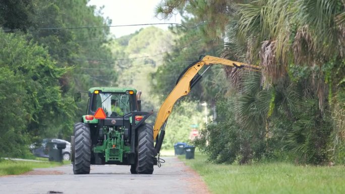 公共工程拖拉机在佛罗里达州乡村街道边修剪树木和绿化树枝