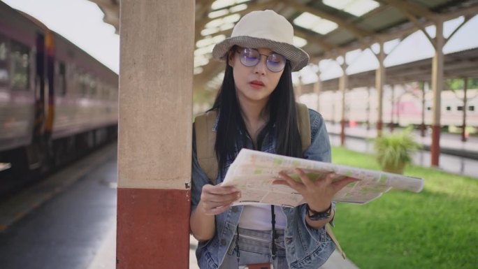 快乐的年轻亚洲女性独自站在火车站，查看纸质地图，找出自己的目的地