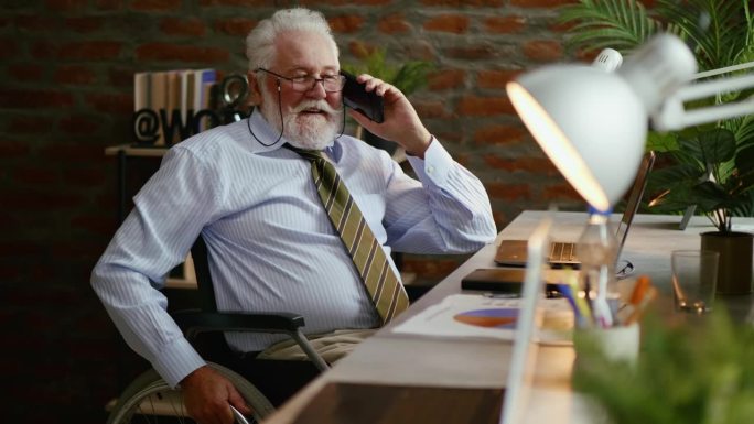 坐在轮椅上的残疾老商人在办公室的办公桌旁打电话