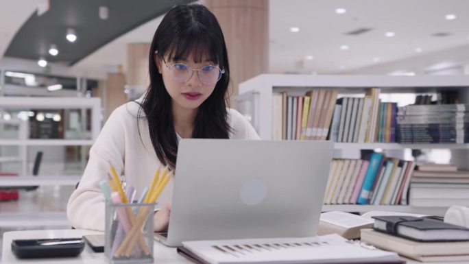 年轻的亚洲女大学生们正在用笔记本电脑认真地完成作业，在网上提交作业，参加网上课程，或在大学图书馆准备