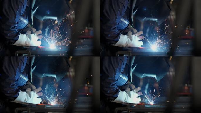 穿着防护服的工程师熟练地焊接钢材，创造出迷人的火花，似乎在跳舞，像一个美丽的奇观。专业是为制造过程做
