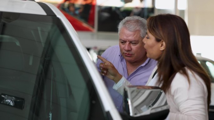 一对成熟的拉丁美洲夫妇在汽车经销店买车，看内饰