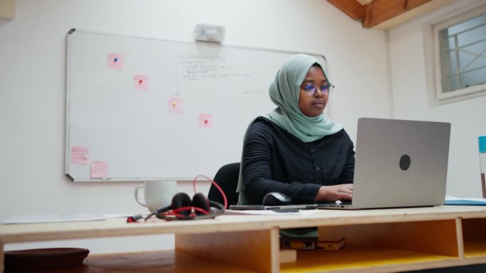 年轻的穆斯林女商人正在用笔记本电脑写笔记