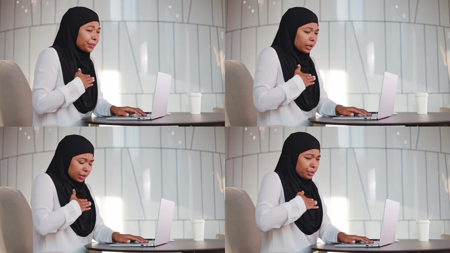 戴着黑色头巾的女商人在明亮的办公大楼里用手提电脑工作时突然胸痛。一位多元文化的女士因工作过度而心脏病
