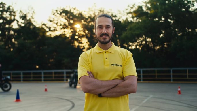 一名穿着黄色t恤、留着胡子的男性驾驶教练将双臂交叉在胸前摆姿势