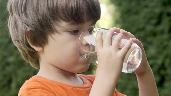 口渴的孩子在阳光照耀的户外喝玻璃水。小孩喝杯新鲜透明纯过滤水慢动作小孩喝杯水健康的身体护理健康的生活
