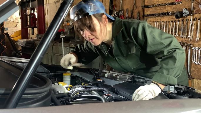 年轻女机械师在修理前用车灯检查汽车发动机