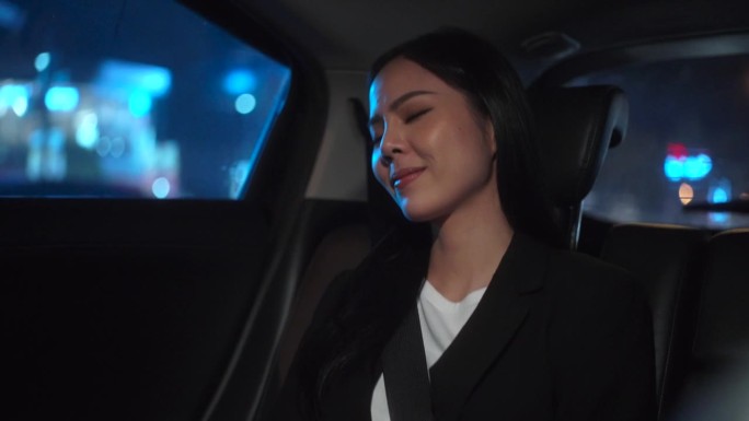 商务女性坐在汽车后座系上安全带，晚上看着窗外的放松感觉。开车的女人在去目的地的路上坐出租车。
