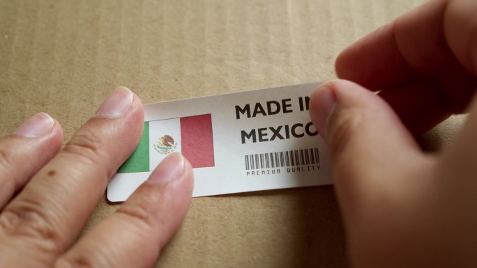 用手将墨西哥制造的旗帜标签贴在带有产品优质条形码的运输箱上。制造和交付。产品出厂进出口。