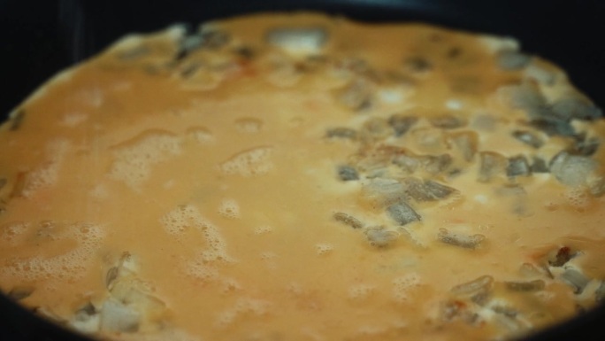 一个延时特写镜头，鸡蛋混合物填满烤洋葱，在黑热的平底锅上翻转煎蛋卷，揉碎鸡蛋，制作早餐4K视频