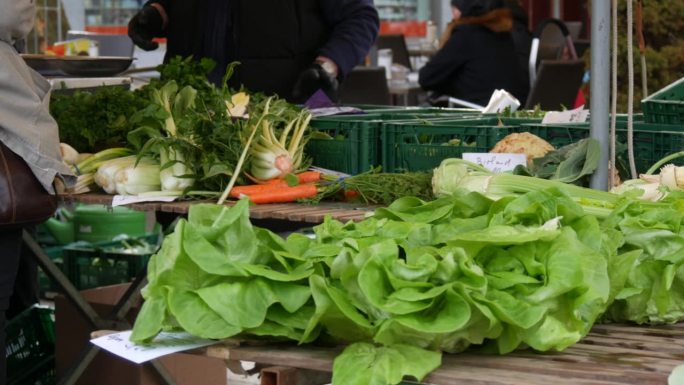 露天市场。买卖双方背景上有各种青菜、沙拉、根、茎。