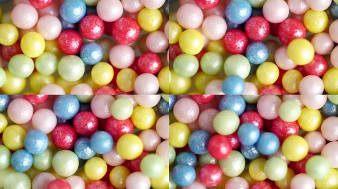 甜甜的糖屑落在其他多色球上，微距视频。五彩缤纷的糖屑旋转，装饰糖球的背景