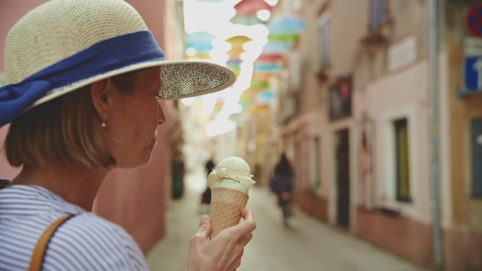在克罗地亚村庄的街道上，女游客在舔冰淇淋，背景是骑自行车的妇女