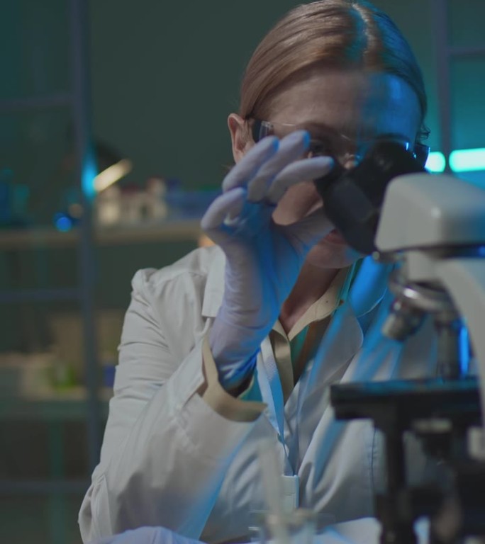 女生化学家在显微镜下检查标本并在笔记本电脑上打字
