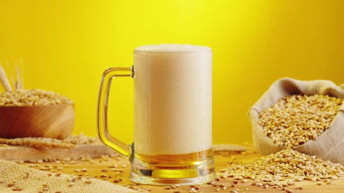 泡沫啤酒在玻璃特写。酒精金色啤酒杯喝。新鲜的淡色麦酒，黄色背景和小麦。