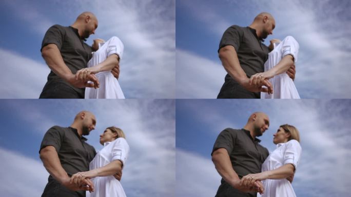 一个男人和一个女人手牵着手，在天空的云的背景下互相欣赏。对焦的手特写，从下往上拍。