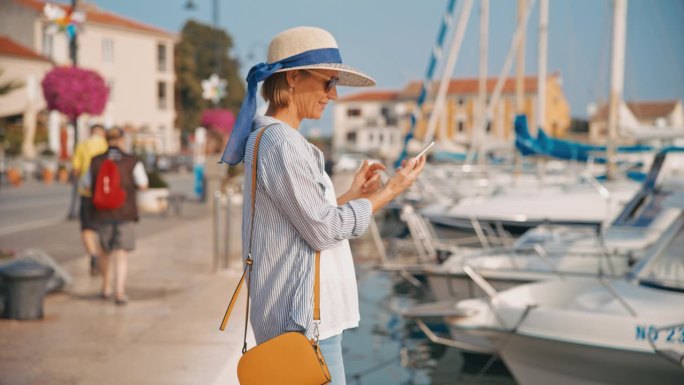 夏季，克罗地亚村庄，站在码头上玩智能手机的快乐女游客