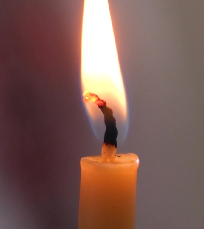 一支白色的蜡烛在燃烧。孤立的蜡烛燃烧与黑暗的背景。白色石蜡蜡烛与黄色阴影燃烧在黑色的背景。纪念或庆祝