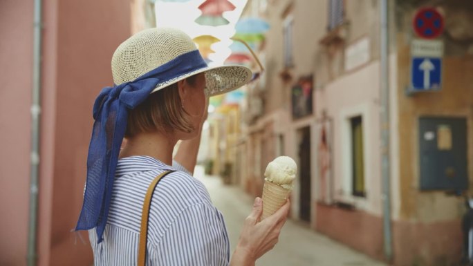 一名女游客走在克罗地亚村庄的街道上，一边吃着新鲜的甜筒冰淇淋