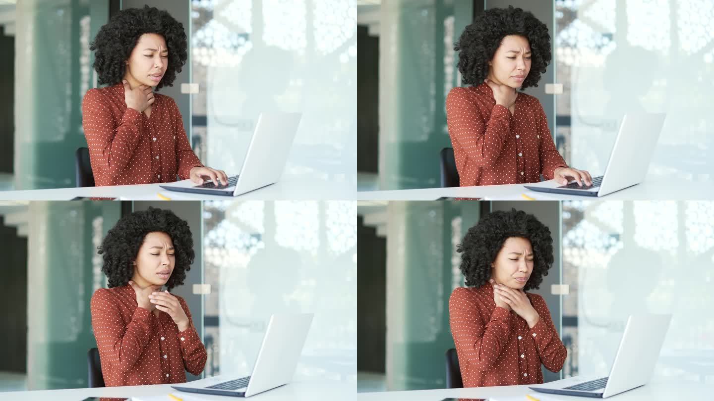 生病的年轻非裔美国女员工在办公室坐着用笔记本电脑工作时喉咙痛