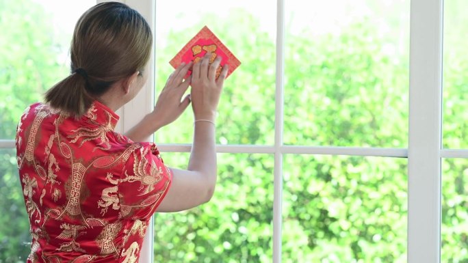 年轻的亚洲女子高兴地在玻璃窗上贴上幸运字来庆祝中国新年