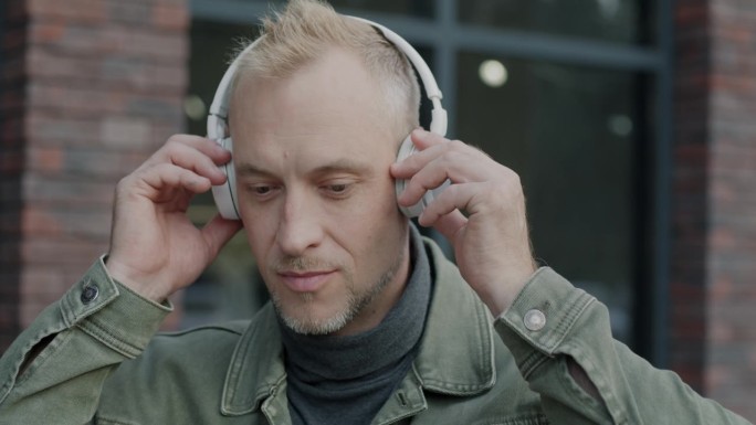 一个欢快的年轻人戴着耳机在城市户外听音乐的特写慢镜头