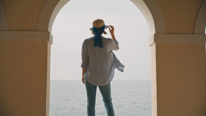 在克罗地亚晴朗的天空下，快乐的女游客拿着遮阳帽站在海边柱廊的挡土墙上
