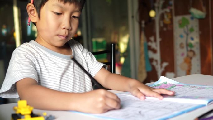小学生在家做作业，神情专注。亚洲小男孩坐在课桌前写练习本。教育理念，学习，家校。