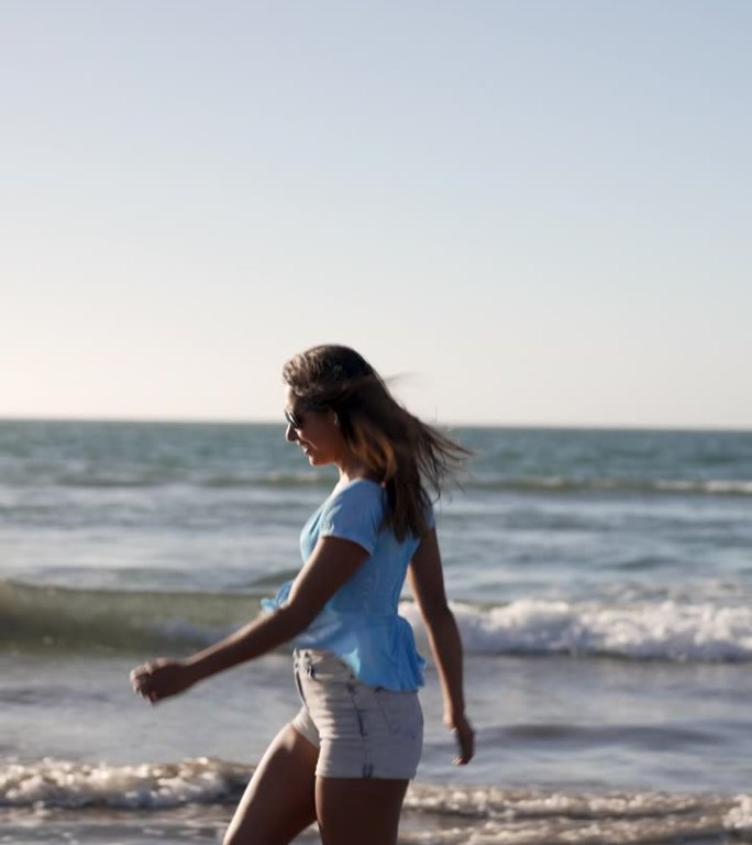 拉丁女人在水里快乐地奔跑，在日落的海滩上听音乐