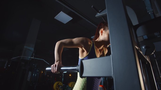 年轻女子在健身房的健身器械上上下拉她的身体，训练双手和肩膀