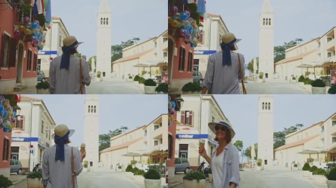 阳光明媚的一天，克罗地亚罗维尼，一名兴高采烈的女游客一边吃着冰淇淋，一边走向大教堂塔
